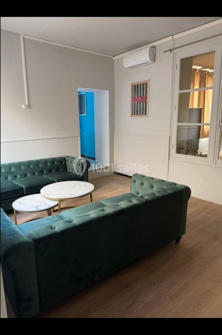 Salon lumineux avec deux canapés verts, tables basses rondes blanches et parquet clair, vue sur une fenêtre et une porte.