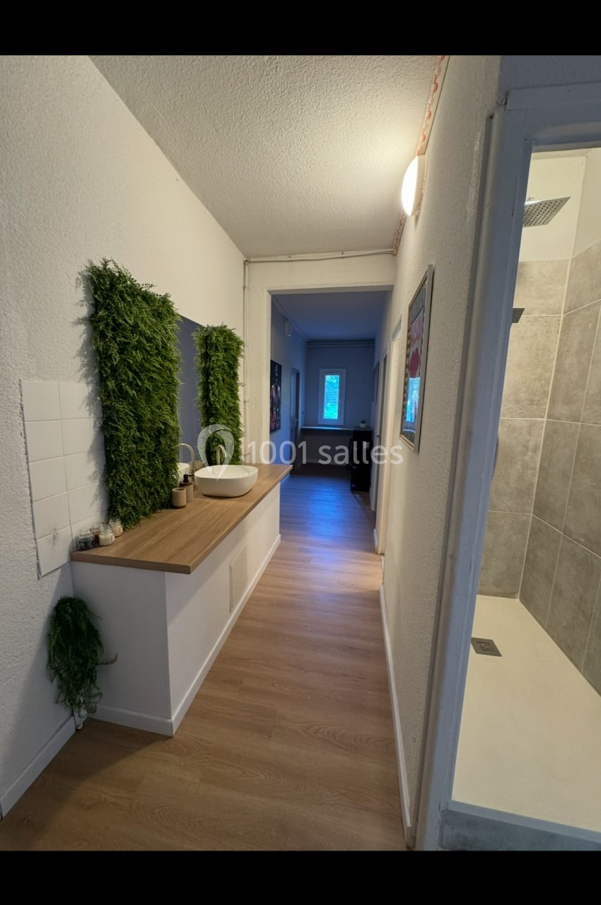 Vue d'un couloir avec un lavabo sur un plan de travail, des plantes murales et une douche à droite.