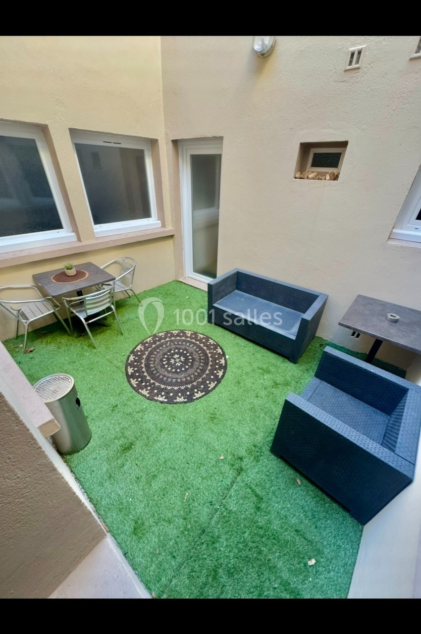 Cour intérieure avec gazon artificiel, mobilier de jardin en rotin, table, chaises et tapis rond décoratif.