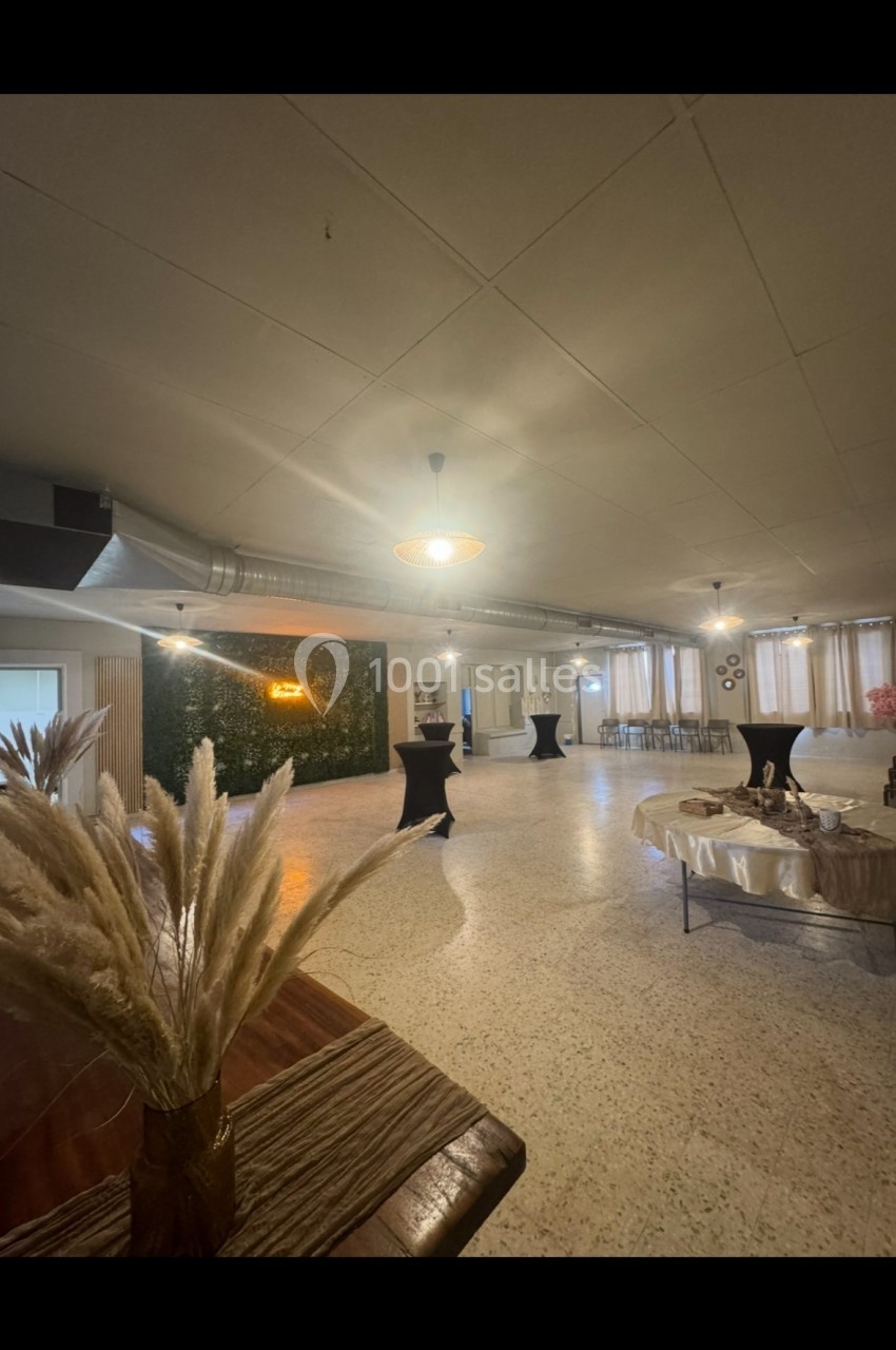 Salle de réception lumineuse avec tables dressées, décorations végétales et espace ouvert pour événements.