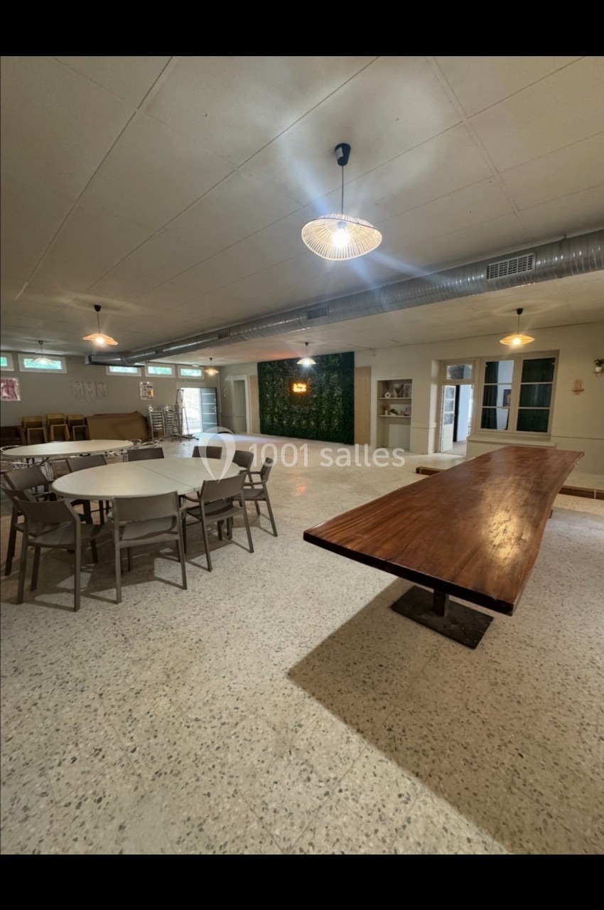 Salle lumineuse avec tables en bois et chaises, sol en terrazzo, mur végétal et éclairage suspendu.