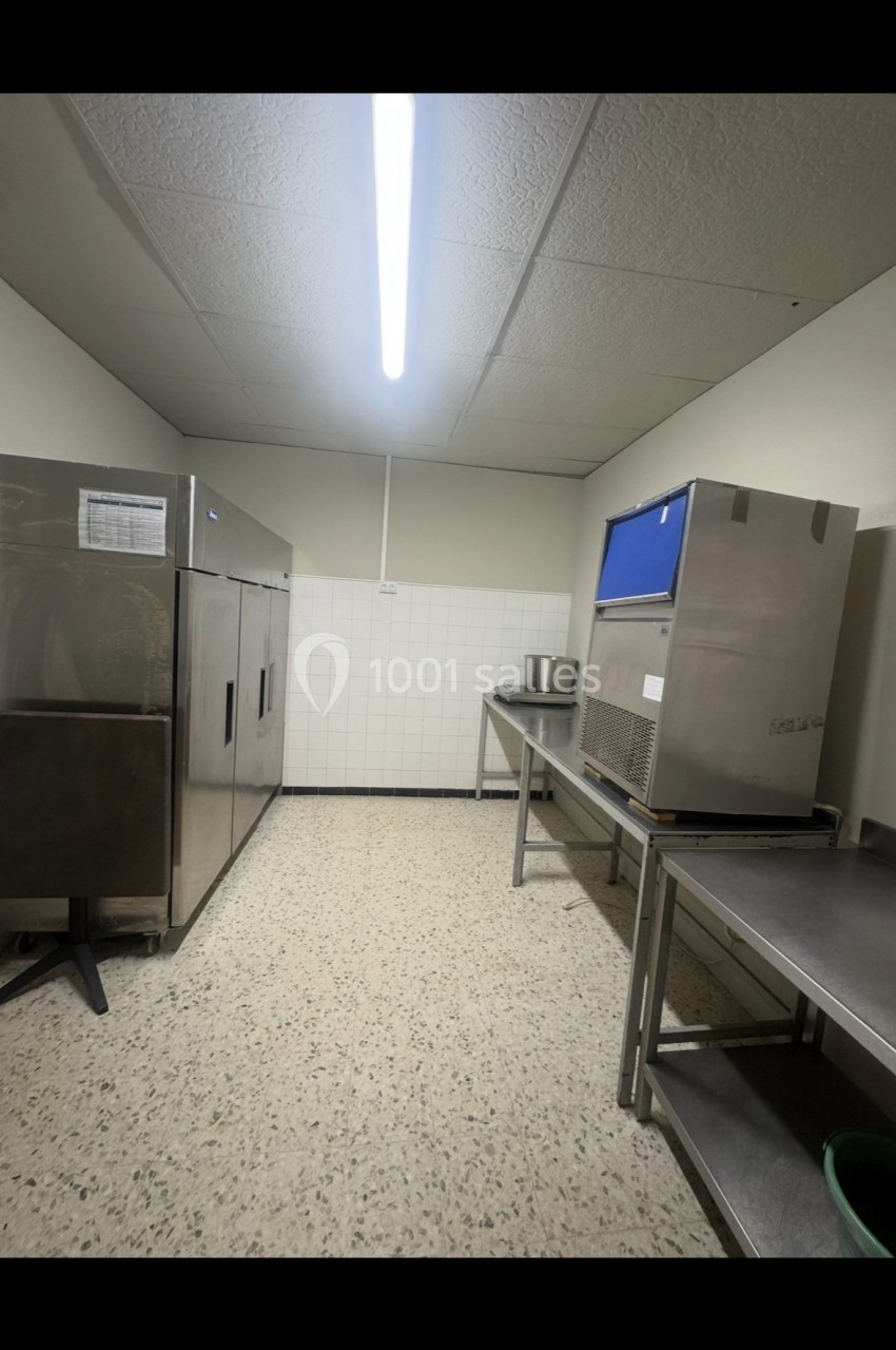 Cuisine professionnelle avec équipements en inox, réfrigérateurs, plan de travail et sol en carrelage clair.