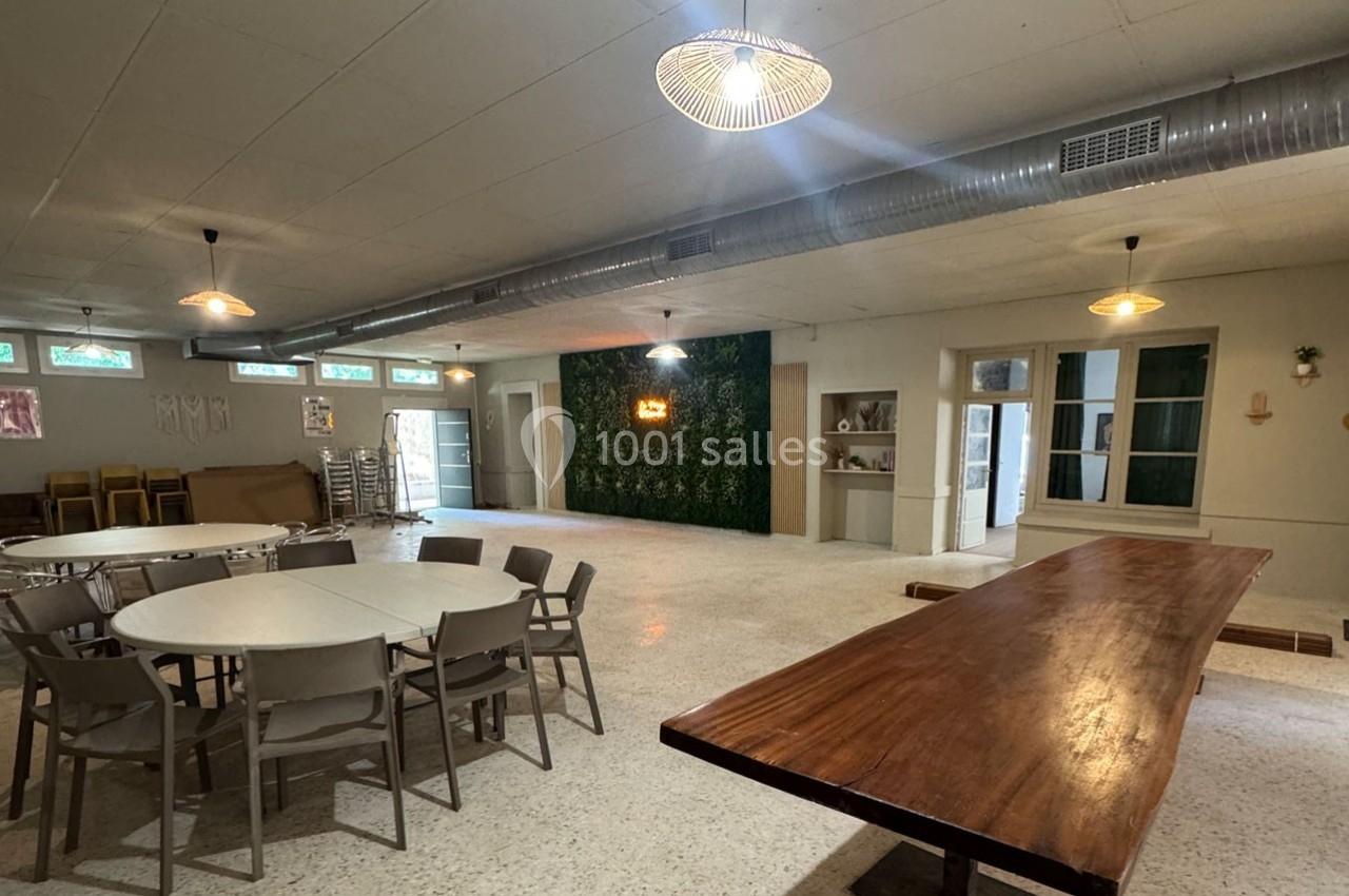 Salle lumineuse avec tables, chaises, mur végétal éclairé et décorations minimalistes dans un espace polyvalent.
