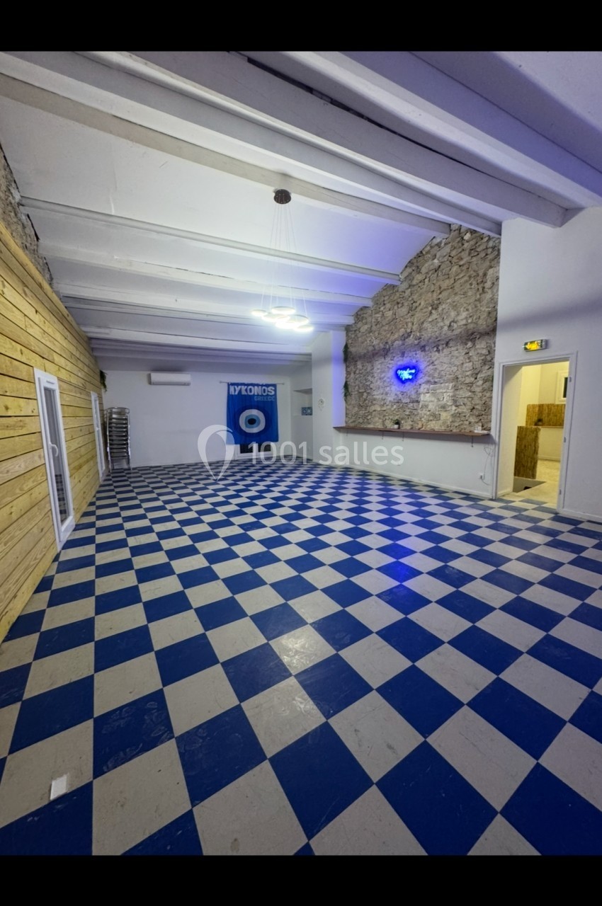 Salle vide avec sol en damier bleu et blanc, murs en bois et pierre, éclairage au plafond et porte ouverte sur la droite.