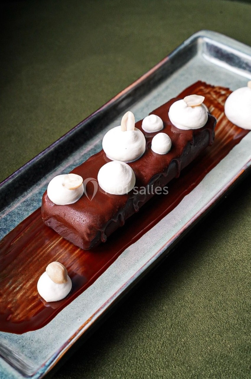 Dessert rectangulaire au chocolat, décoré de meringues et d'amandes, présenté sur une assiette rectangulaire.