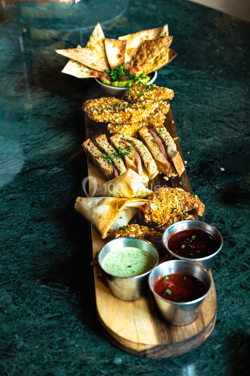 Plateau en bois garni de snacks variés, sauces en ramequins, sur une table sombre.