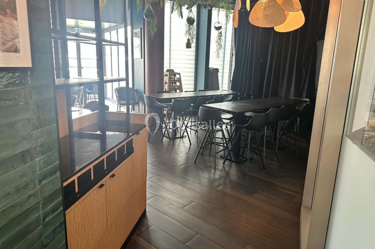 Salle de restaurant moderne avec tables noires, chaises assorties, luminaires suspendus et décorations végétales.