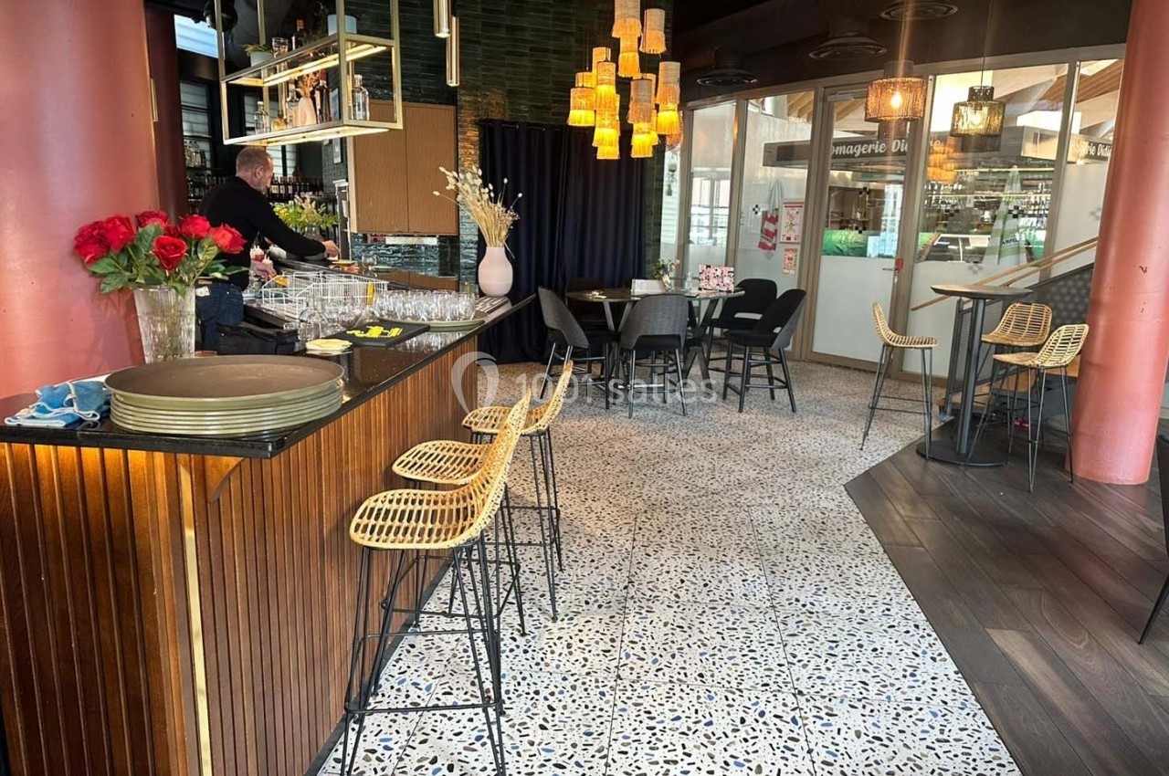 Intérieur d'un café moderne avec un bar en bois, des tabourets en rotin, des tables et des luminaires suspendus.