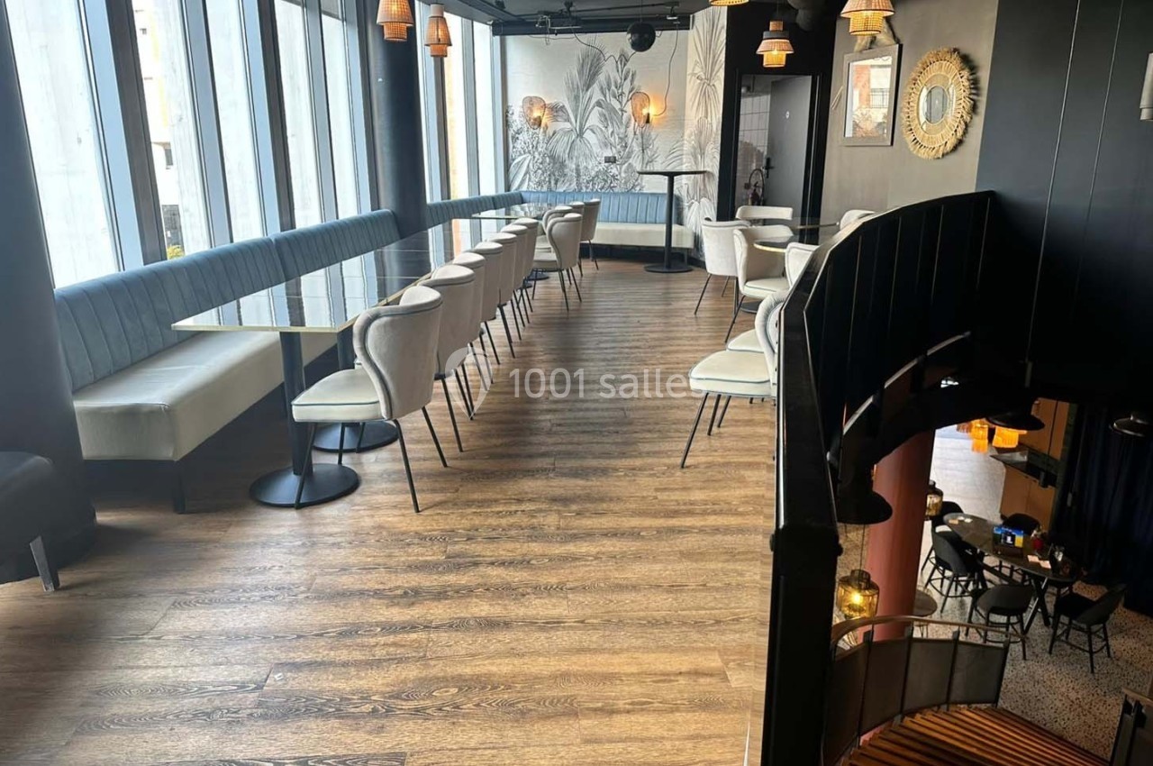Salle de restaurant moderne avec parquet en bois, banquettes bleues, chaises claires et grandes fenêtres laissant entrer la…