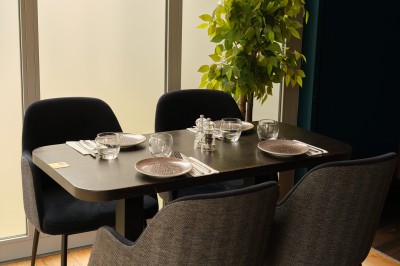 Miniature Location salle Courbevoie (Hauts-de-Seine) - Verrä #12 Table dressée pour quatre personnes avec assiettes, couverts et verres, près d'une plante et d'une baie vitrée.