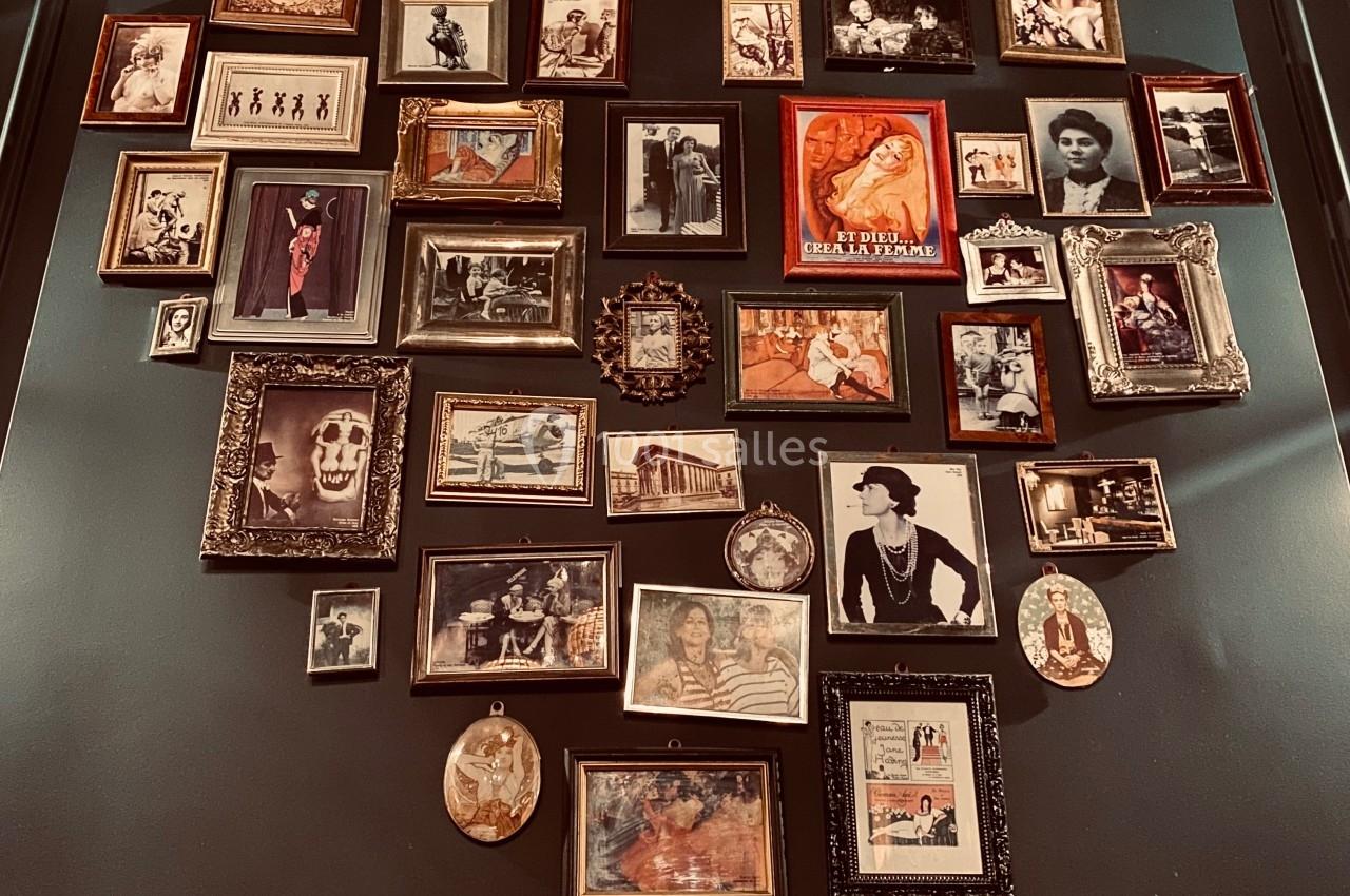 Mur décoré de cadres photo anciens de tailles variées, disposés en forme de cœur sur un fond sombre.