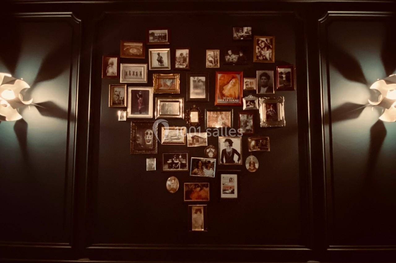 Mur décoré de cadres photos variés, éclairé par deux appliques murales, au-dessus d'une banquette à motifs géométriques.