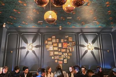 Salle de restaurant cosy avec fauteuils imprimés, éclairage tamisé et plafond décoré de motifs floraux.