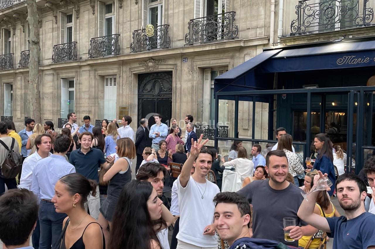 Groupe de personnes discutant et socialisant devant un bâtiment haussmannien avec balcons en fer forgé.