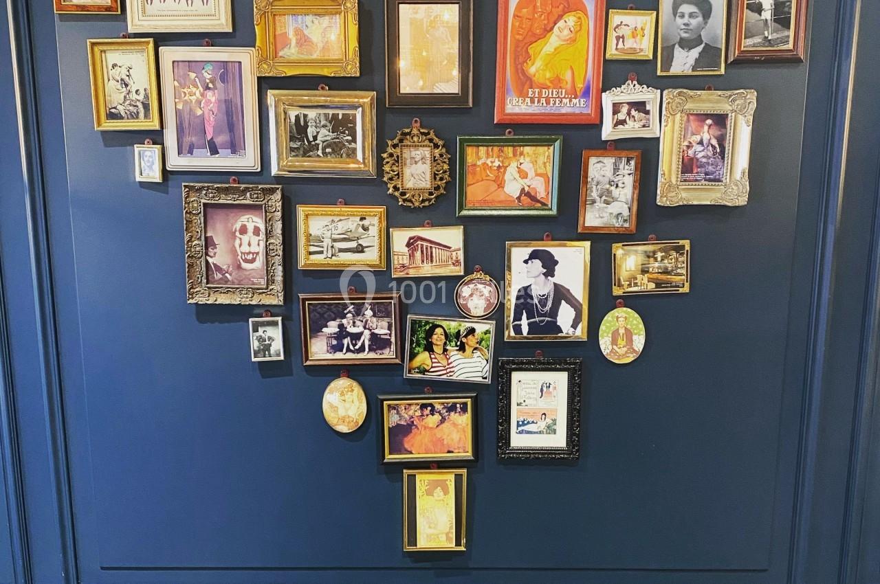 Mur bleu décoré de cadres photo de tailles variées, formant une composition artistique au-dessus d'un sol à motifs…