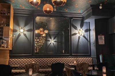 Salle de restaurant cosy avec fauteuils imprimés, éclairage tamisé et plafond décoré de motifs floraux.