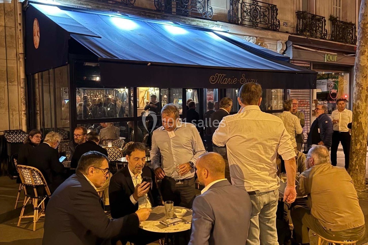 Groupe de personnes discutant et partageant des boissons en terrasse d'un café animé en soirée.