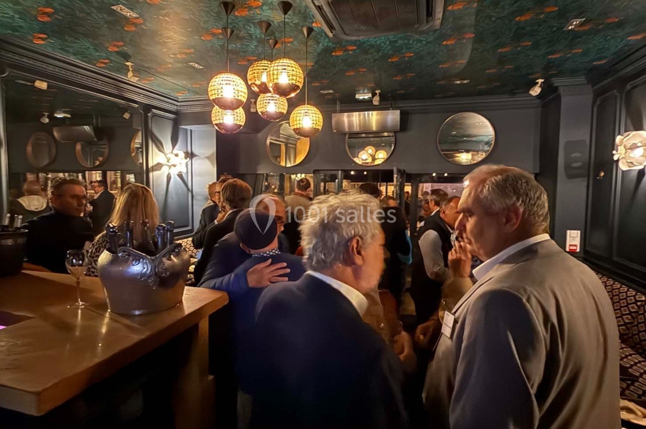 Groupe de personnes discutant dans un bar à l'ambiance tamisée, avec des miroirs et des luminaires décoratifs.
