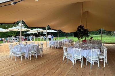 Groupe de personnes assises en extérieur lors d'une cérémonie, entourées d'arbres et de fleurs sous un ciel partiellement…