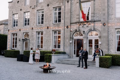 Groupe de personnes rassemblées sous une tente beige sur une terrasse en bois, dans un jardin arboré.