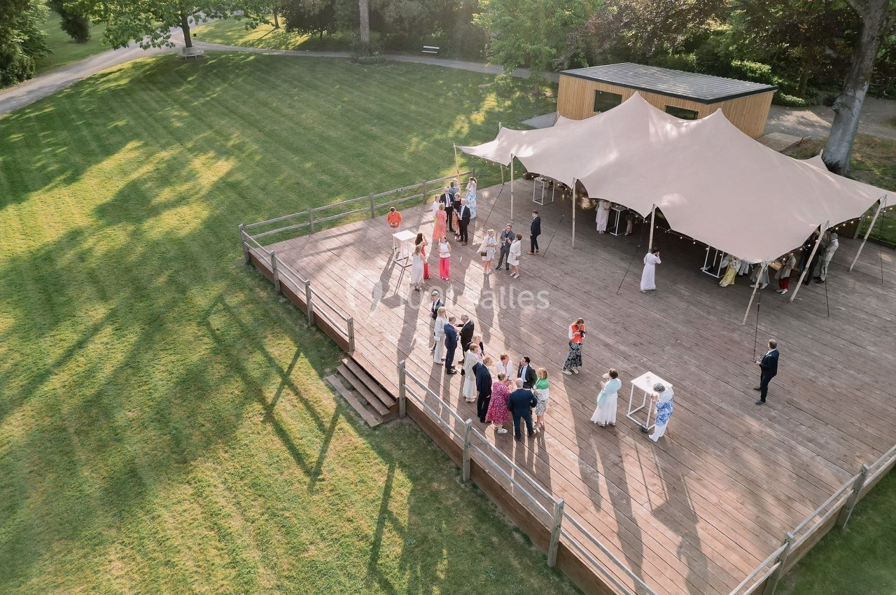 Vue aérienne d'un groupe de personnes rassemblées sur une terrasse en bois, entourée d'une pelouse et d'arbres.