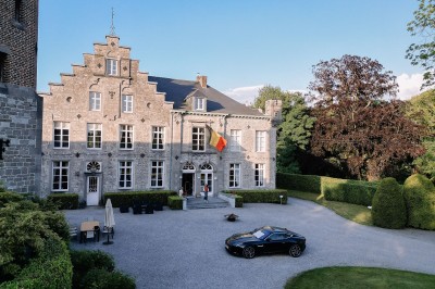 Groupe de personnes rassemblées sous une tente beige sur une terrasse en bois, dans un jardin arboré.