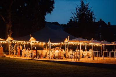 Dîner en plein air sous des guirlandes lumineuses, avec des invités assis autour de tables éclairées au crépuscule.
