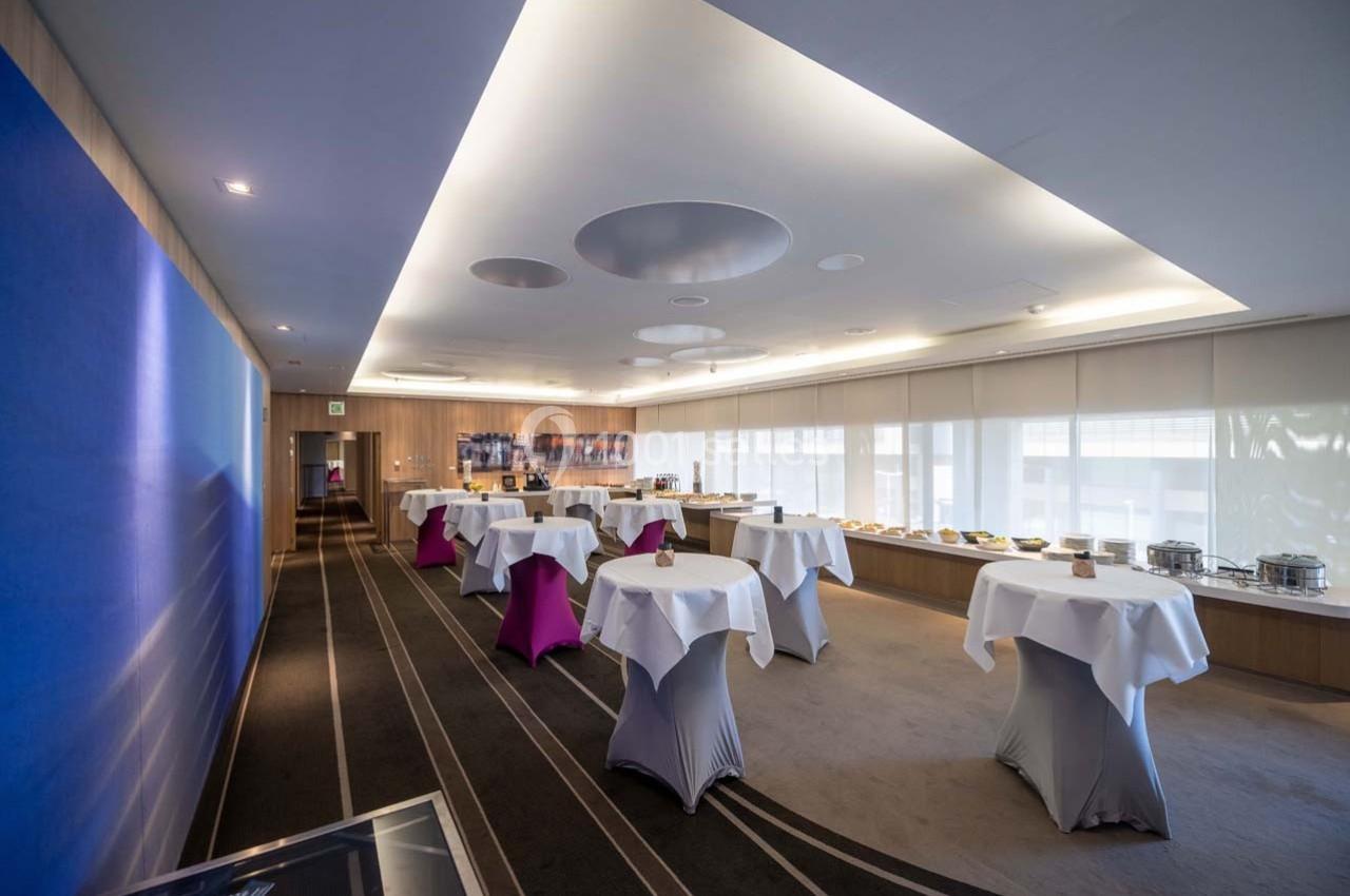 Salle de réception lumineuse avec tables hautes recouvertes de nappes blanches et buffet disposé le long du mur.