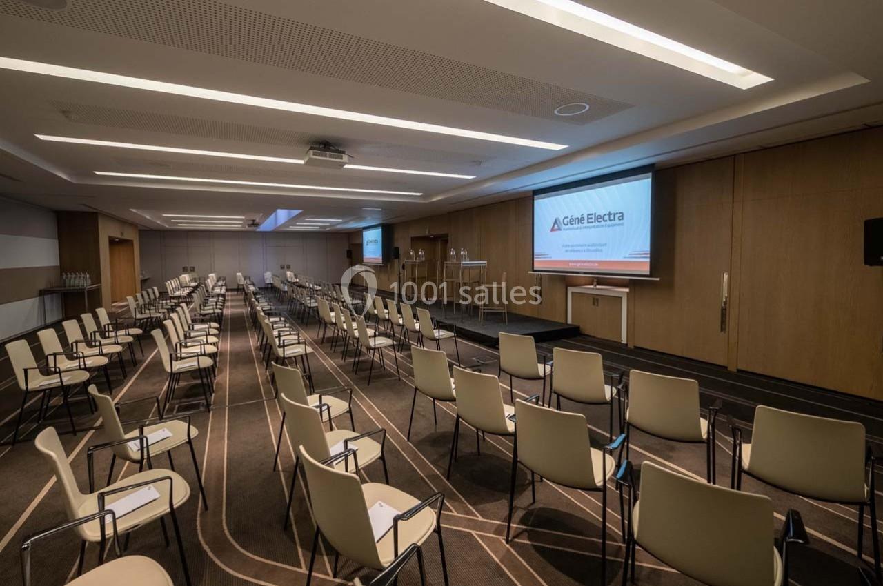 Salle de conférence moderne avec chaises alignées, écran de projection allumé et éclairage tamisé.