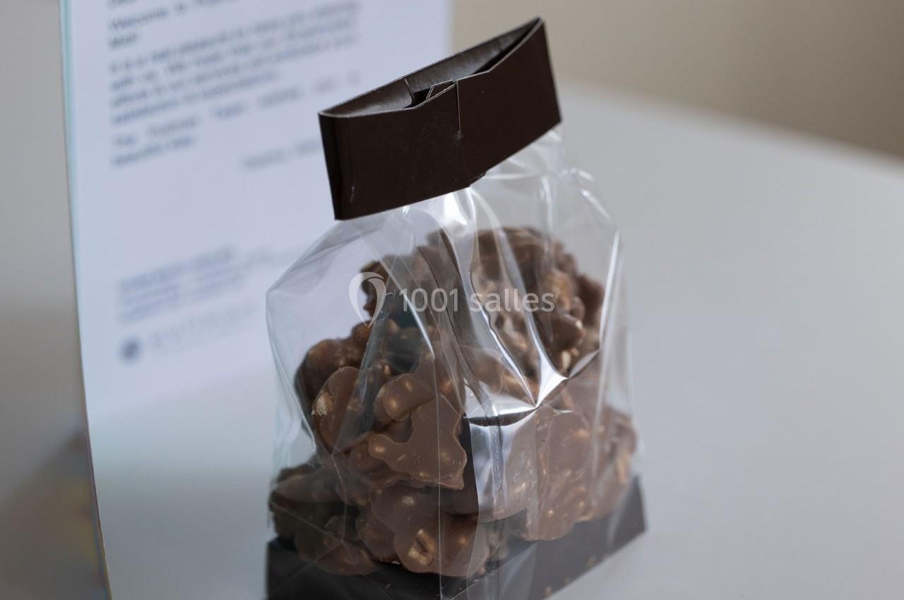 Sachet transparent contenant des morceaux de chocolat au lait avec des éclats de noix, posé sur une surface blanche.