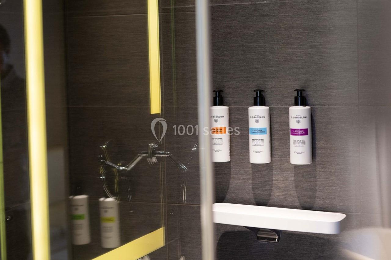 Trois distributeurs de savon fixés sur un mur de douche sombre, avec un éclairage jaune en reflet.