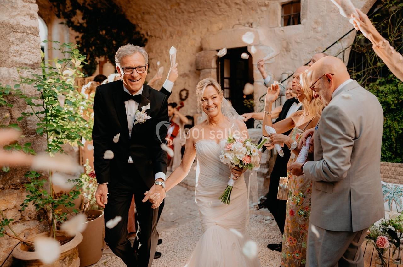 Un couple souriant sort d'une cérémonie de mariage sous une pluie de pétales, entouré d'invités joyeux.