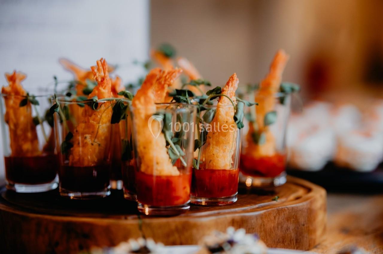 Crevettes panées servies dans des verrines avec une sauce rouge et garnies de micro-pousses.