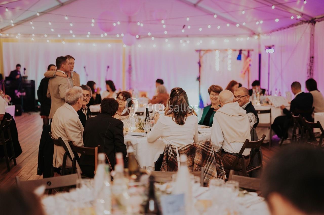 Des invités assis autour de tables décorées dans une tente éclairée par des guirlandes lumineuses lors d'un événement.