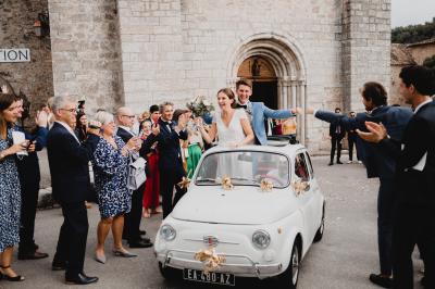 Un couple souriant marche main dans la main au milieu d'invités applaudissant lors d'une cérémonie en plein air.