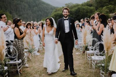 Un couple souriant marche main dans la main au milieu d'invités applaudissant lors d'une cérémonie en plein air.