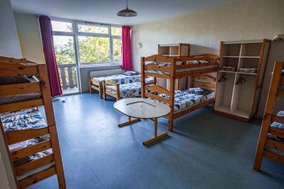 Deux lits simples avec couvre-lits bleus, une lampe de chevet, un bureau et un lavabo dans une chambre lumineuse.