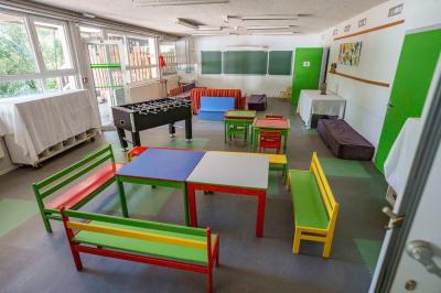 Deux lits simples avec couvre-lits bleus, une lampe de chevet, un bureau et un lavabo dans une chambre lumineuse.