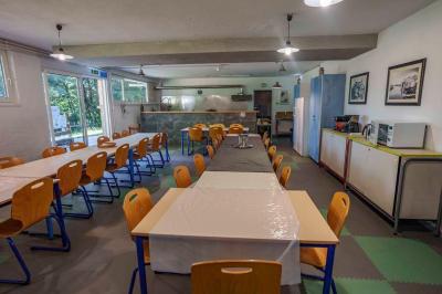 Deux lits simples avec couvre-lits bleus, une lampe de chevet, un bureau et un lavabo dans une chambre lumineuse.