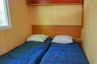 Deux lits simples avec couvre-lits bleus, une lampe de chevet, un bureau et un lavabo dans une chambre lumineuse.