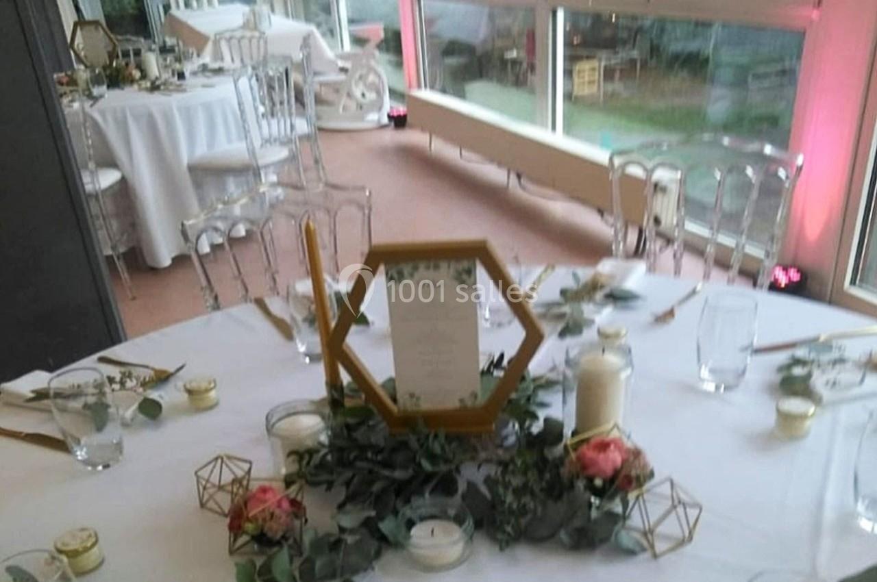 Table de réception décorée avec des bougies, des fleurs roses, des feuillages et un menu dans un cadre hexagonal.