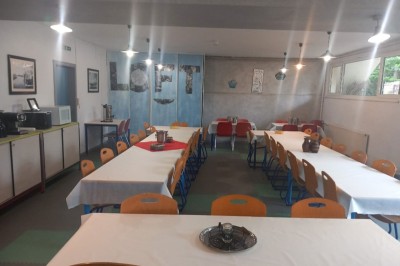 Deux lits simples avec couvre-lits bleus, une lampe de chevet, un bureau et un lavabo dans une chambre lumineuse.