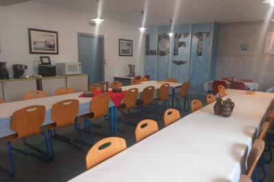 Deux lits simples avec couvre-lits bleus, une lampe de chevet, un bureau et un lavabo dans une chambre lumineuse.