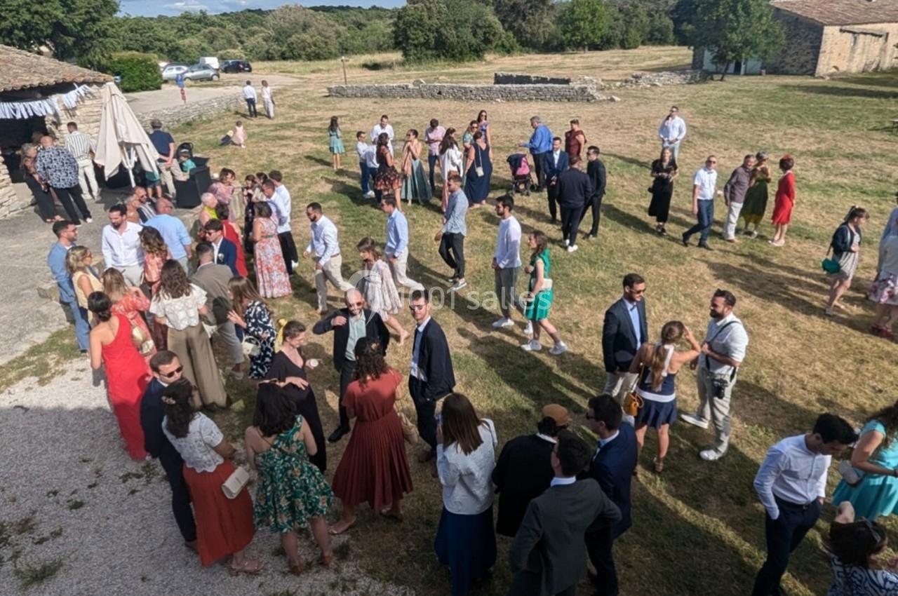 Groupe de personnes rassemblées en extérieur dans une cour herbeuse, discutant par petits groupes sous un ciel dégagé.