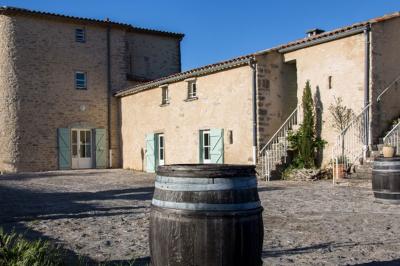 Cour pavée avec des bâtiments en pierre, volets pastel, barils en bois et escalier extérieur sous un ciel bleu.