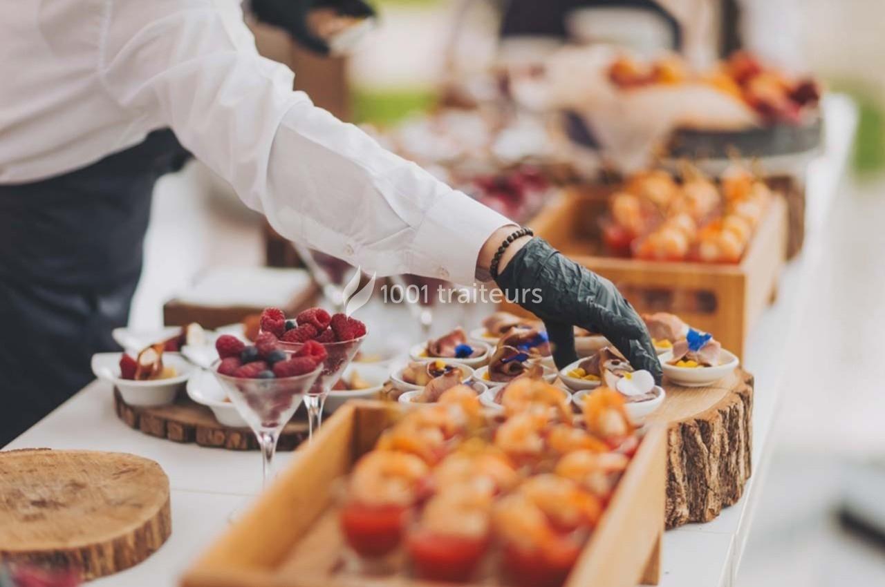 Une main gantée dispose des amuse-bouches sur une table garnie de verrines et de petites assiettes.