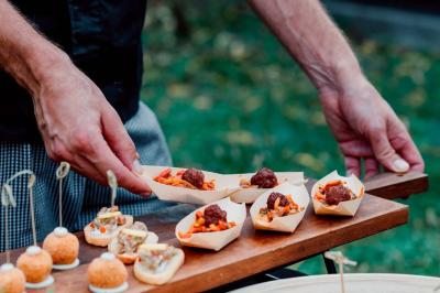 Un serveur présente des amuse-bouches dans des barquettes en bois, composés de boulettes de viande et de garnitures colorées.