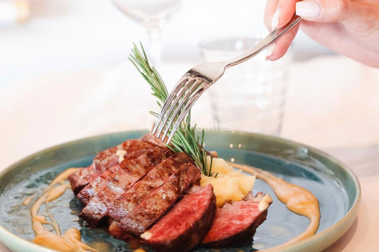 Assiette contenant un steak saignant tranché, accompagné de purée, sauce et décoré d'une branche de romarin.