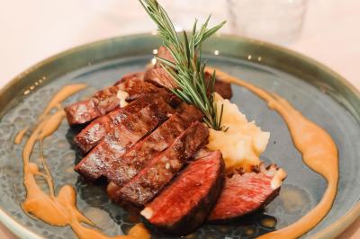 Salle de restaurant lumineuse avec tables dressées, chaises rembourrées, mur décoré de bouteilles de vin et lustre suspendu.
