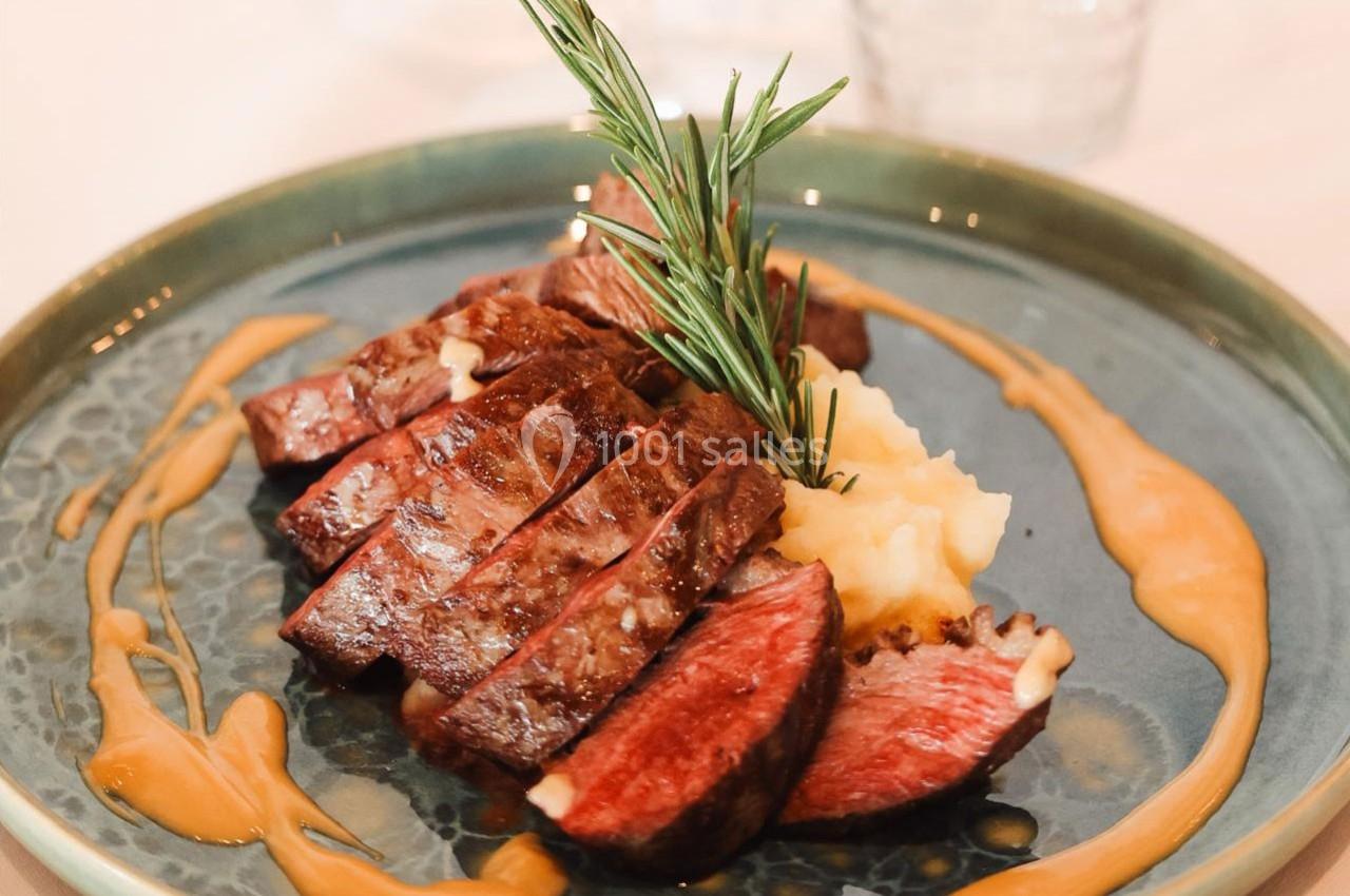 Assiette de steak tranché avec purée de pommes de terre, sauce et garniture de romarin sur une assiette verte.